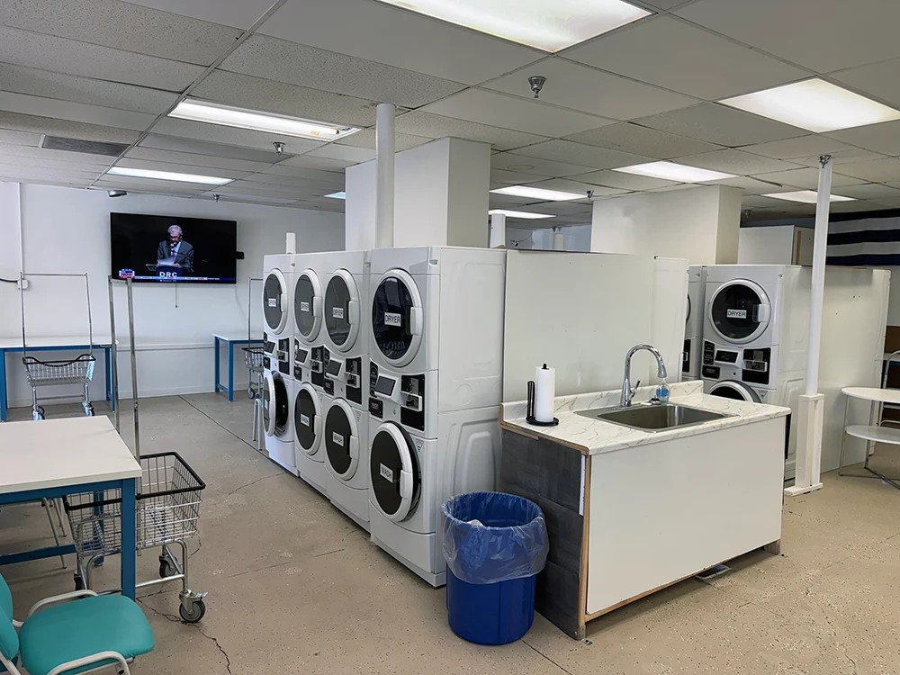 Dryers, tables, and seating area with TV and vending machines.